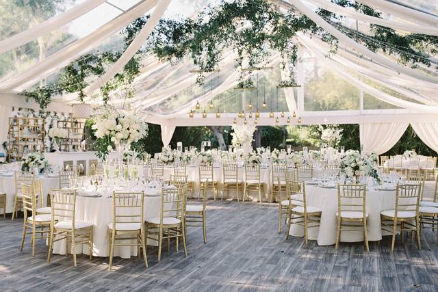 Wedding reception tent decorated with greenery, flowers and gold chairs